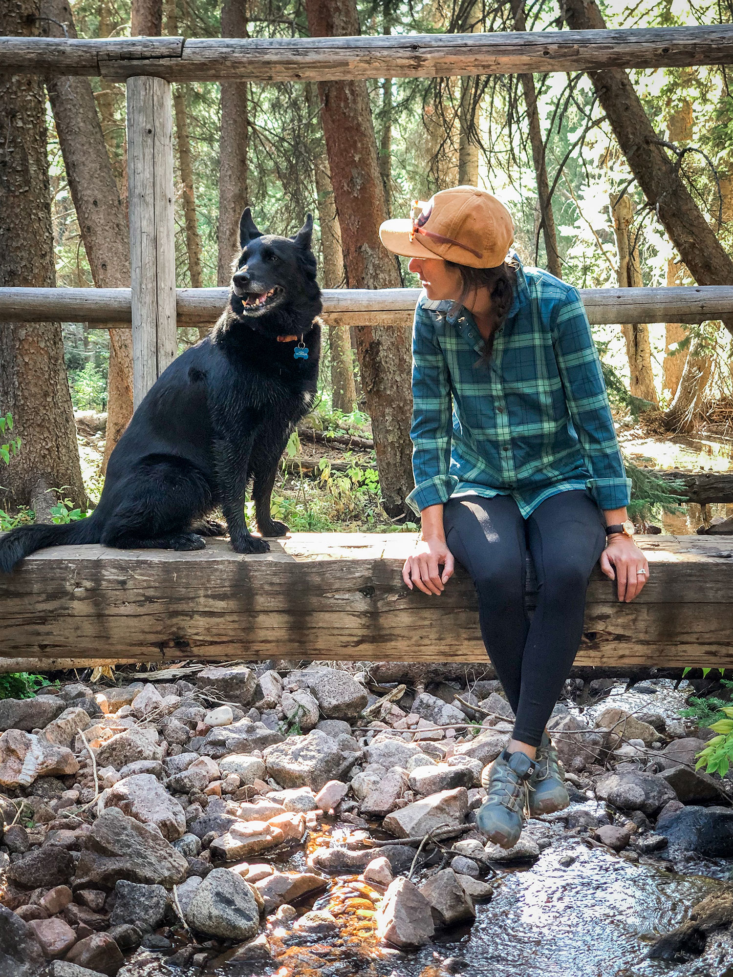 woman sitting on wood bridge with black dog