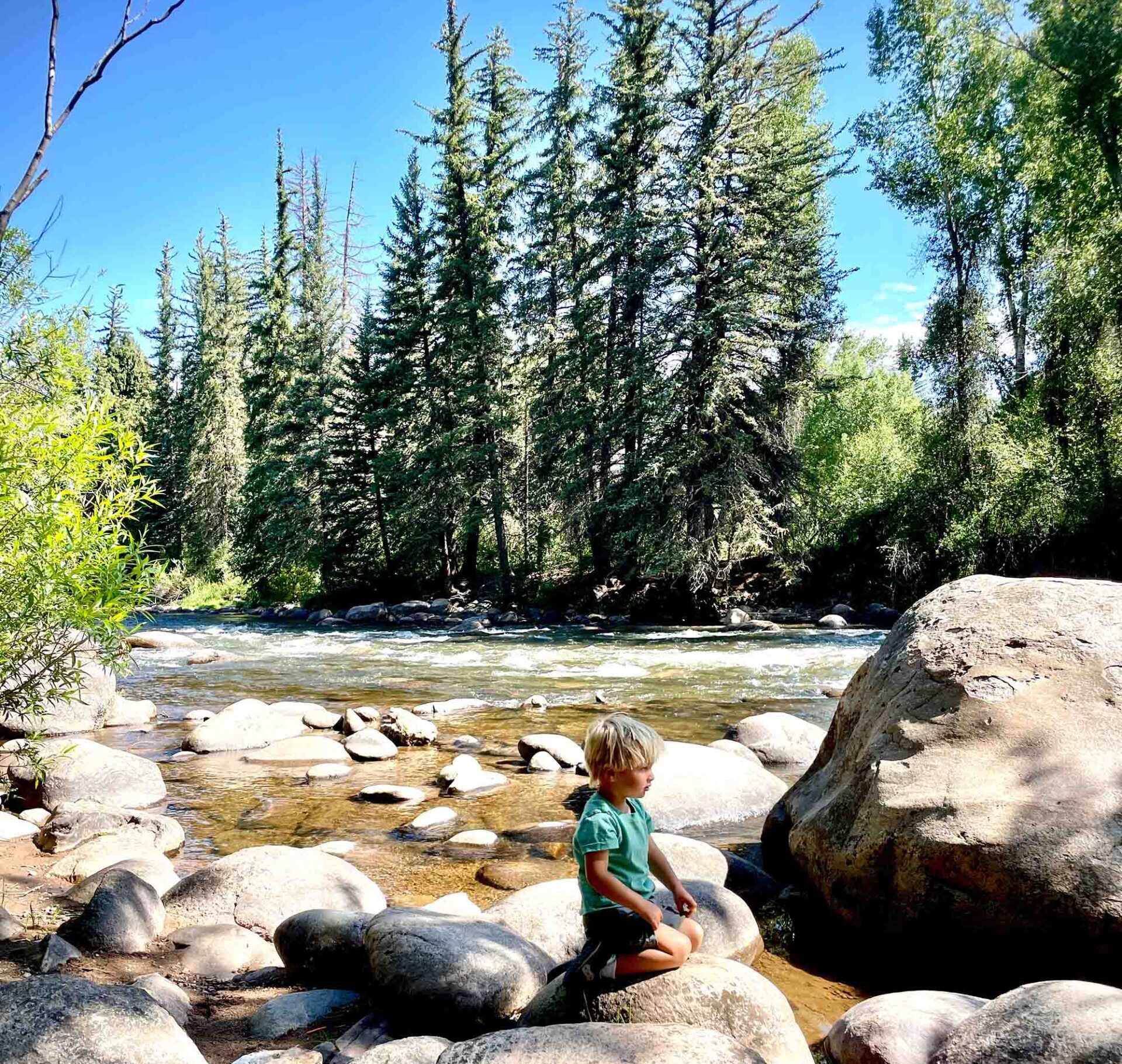 young blond boy sitting on a rock by the river in vail colorado